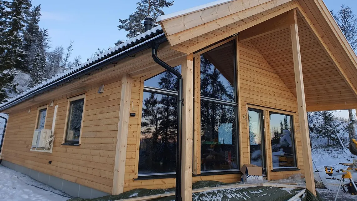 Moderne ny hytte med skråtak og store vindu i snødekt skog