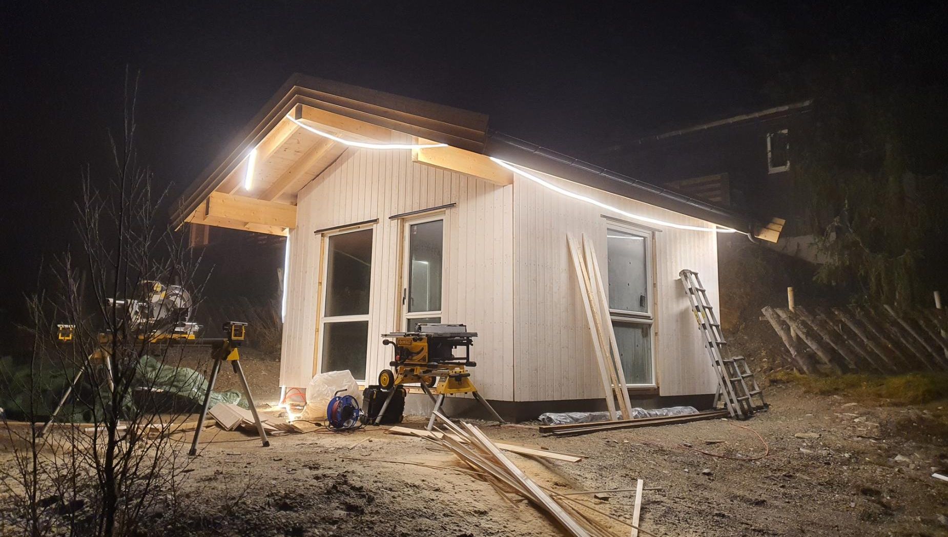 Lite bygg under oppføring med arbeidslys montert i takutstikk og byggeutstyr plassert rundt.