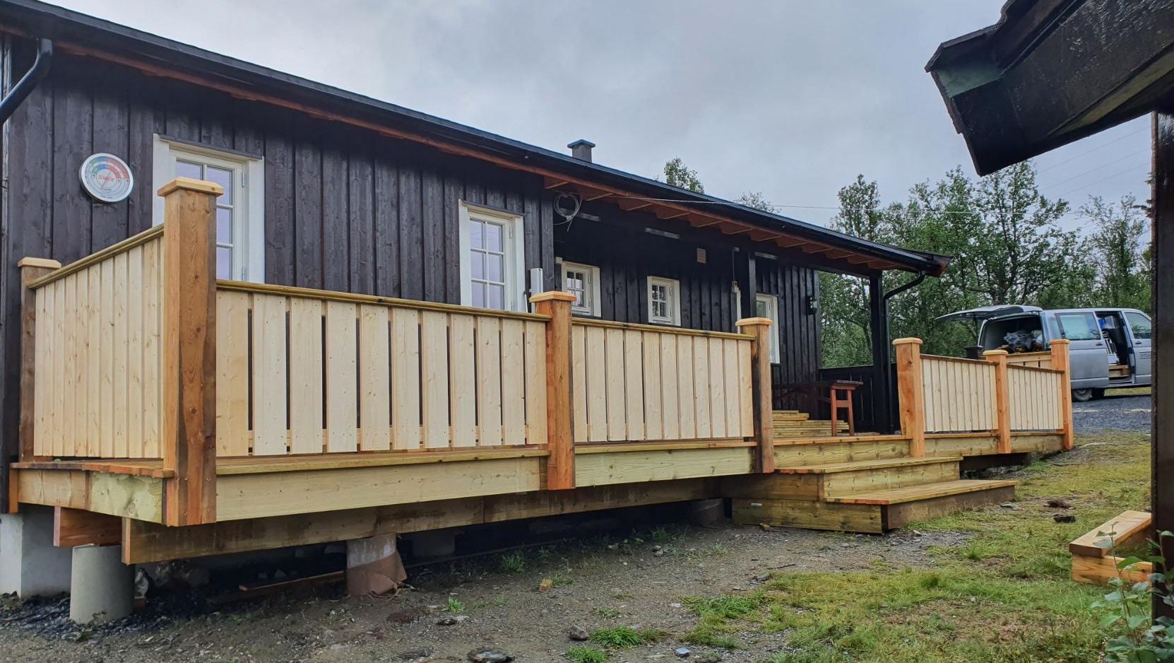 Mørk hytte i tre med ny platt og trapp med sollid trerekkverk