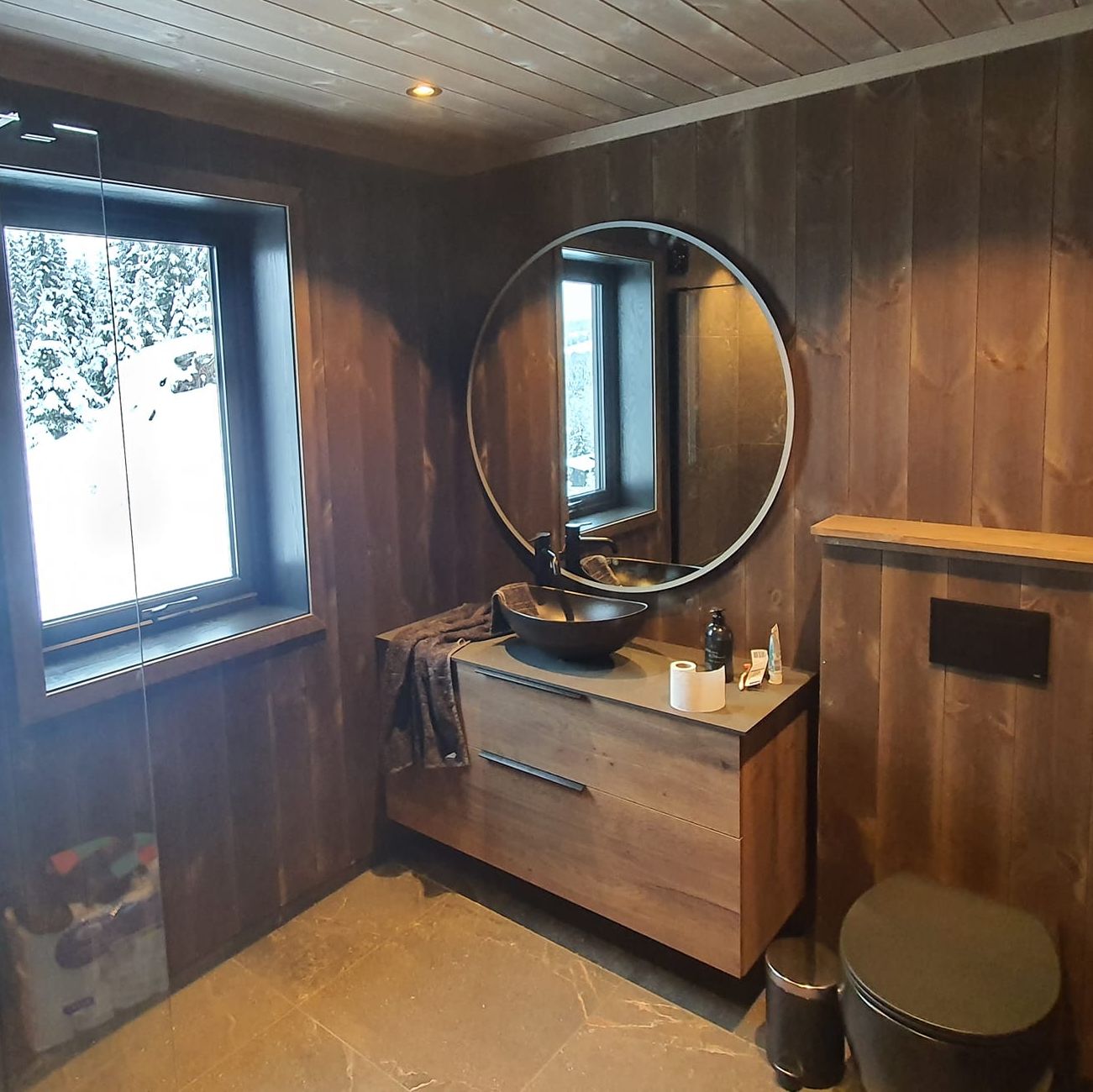 Moderne bad i mørkt tre med vindu og utsikt til snødekt skog