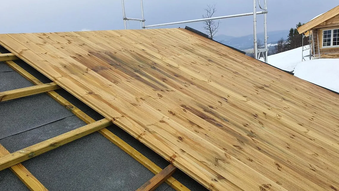 Påbegynt tretak med undertak og lekter, med snødekt landskap og stillas i bakgrunnen.