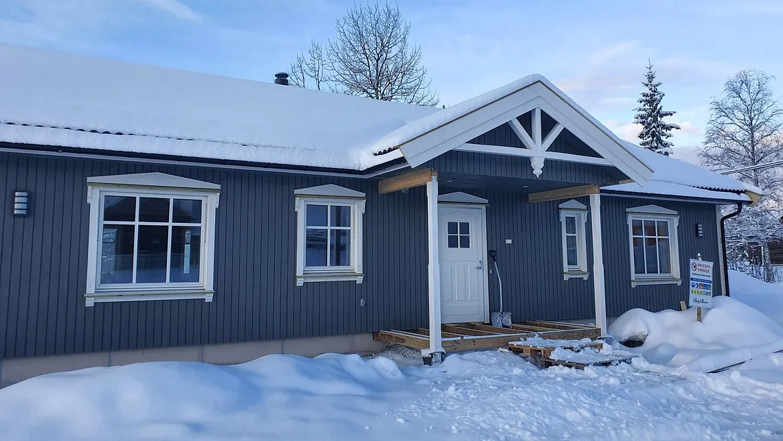 Blå hytte med hvite detaljer i snølandskap